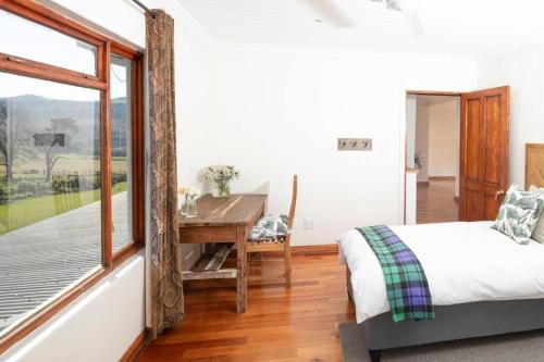 a bedroom with a bed and a desk and a window at The Loop Farmhouse Mooi River in Mooirivier