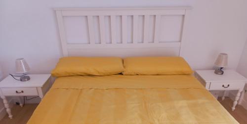 a bed with yellow sheets and two white tables at Aroa's Home -Sirimiri Apartments- in Zumaia