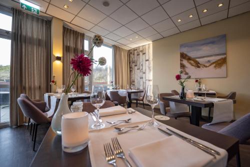 a restaurant with white tables and chairs and a table with red flowers at Fletcher Hotel Restaurant Zeeduin in Wijk aan Zee