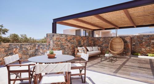 a patio with a table and chairs and a stone wall at St. Nicolas Bay Resort Hotel & Villas in Agios Nikolaos