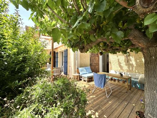 une terrasse en bois avec un banc, une table et un arbre dans l'établissement Le Cocon, Appartement pour 2 personnes à 5 minutes de la plage de l'Almanarre à Hyères, à Hyères