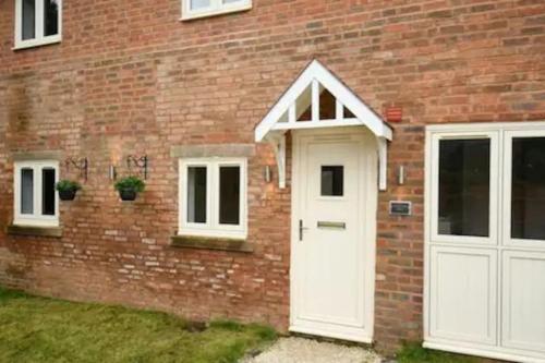 a brick house with a white door and two windows at Newly Converted Barn in Kings Bromley