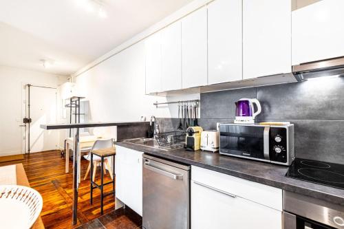une cuisine avec des armoires blanches et un micro-ondes dans l'établissement GuestReady - Appartement Confortable dans le 10e., à Paris