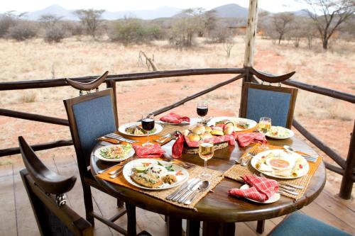 Samburu Sopa Lodge في Archers Post: طاولة مع طعام وكؤوس من النبيذ على شرفة