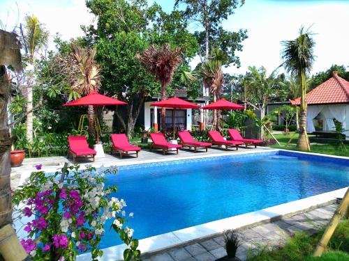 a swimming pool with chairs and red umbrellas at D'Mell Bali in Nusa Dua