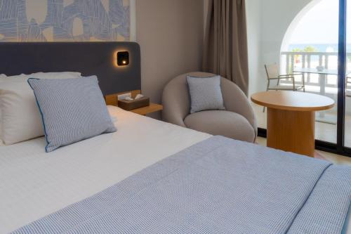 a bedroom with a bed and a chair and a window at Royal Tulip Taj Sultan in Hammamet
