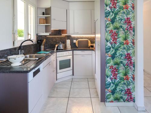 a kitchen with white cabinets and a tropical wallpaper at Villa Route de la Muraz 9 by Interhome in Villeneuve