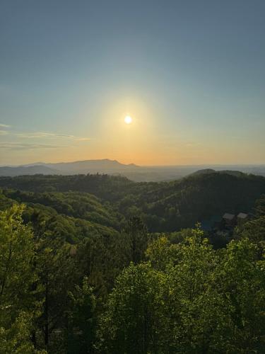 a view of the sun setting over the trees at New Luxury Cabin with Stunning MountainVIEWS,HotTub, FirePit, FirePlace,2 KingBeds, 2 CoveredDecks,BBqGrill, ShuffleBoard and Pool Access in Sevierville