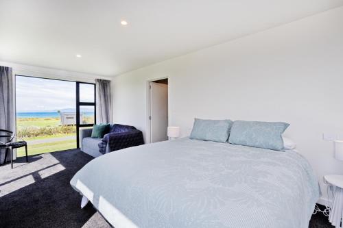 a white bedroom with a bed and a chair at Southern Breeze - Colac Bay Beach House in Riverton