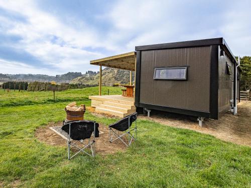 a small shed with two chairs in the grass at Whare Awa - River House in the Rangitīkei in Hunterville