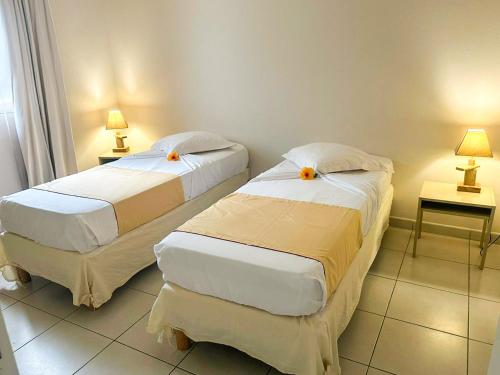 two beds in a room with two tables and two lamps at Hôtel Village Pomme Cannelle 3 étoiles in Le Prêcheur