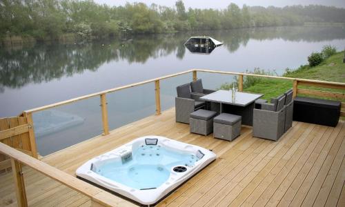 a deck with a hot tub and a table on a lake at Rolo's Lakeside Lodge With Hot Tub & Hi-Speed Wifi in Stamford