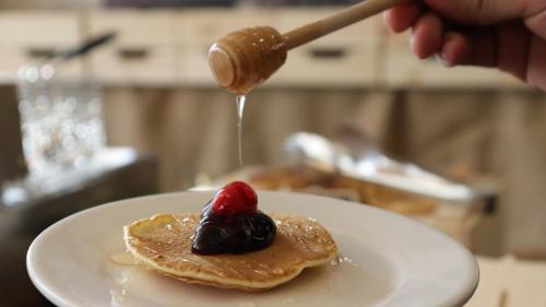a person is drizzling syrup on a plate with pancakes with a raspberry at Sandy palace Hotel in Amman