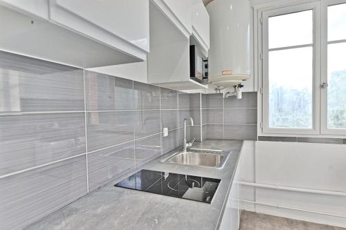 une cuisine blanche avec un évier et une fenêtre dans l'établissement Appartement Cosy Vue sur Paris Bois de Boulogne, à Puteaux