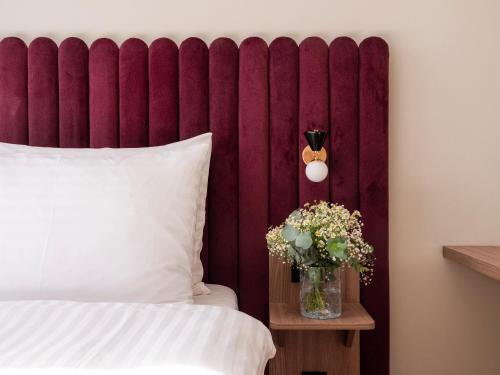 a bed with a red headboard and a vase of flowers at Numa Salzburg Vogelweider in Salzburg