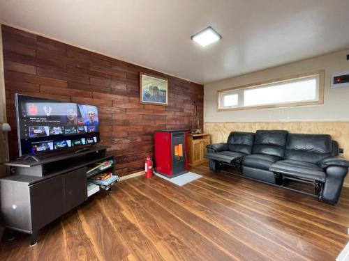 a living room with black leather furniture and a flat screen tv at Cabaña de Lujo en Llau Llao, con agua purificada, confort y bienestar con especial cuidado ambiental, hermosa vista, estratégicamente ubicada entre Castro y Dalcahue in Tentén