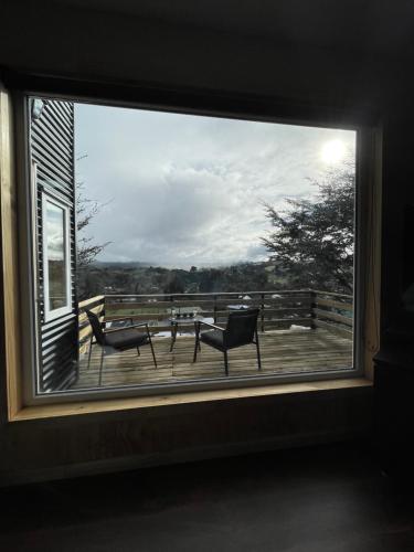 a window with a view of a table and chairs on a deck at Cabaña de Lujo en Llau Llao, con agua purificada, confort y bienestar con especial cuidado ambiental, hermosa vista, estratégicamente ubicada entre Castro y Dalcahue in Tentén