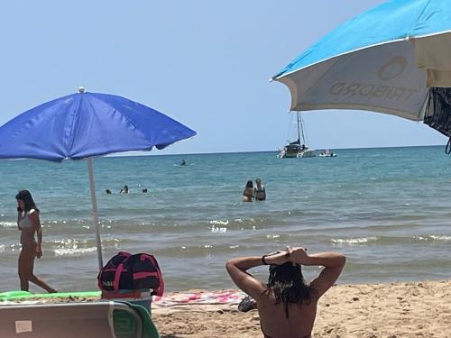 a woman sitting on the beach under a blue umbrella at AMarescaladeiturchy Scaladeiturch in Realmonte