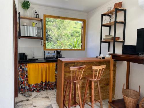 a kitchen with a bar with stools and a window at Chalés São João - a 500m da Cachoeira de Bom Jardim - com piscina in Mutum