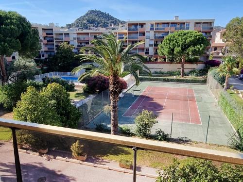 un court de tennis avec un palmier en face d'un bâtiment dans l'établissement Le Repaire des Palmiers - T2 en centre-ville avec parking et piscine, à Hyères