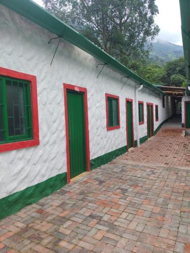 a white building with red and green doors and a brick sidewalk at Casa Flórez Hotel Campestre in Ibagué