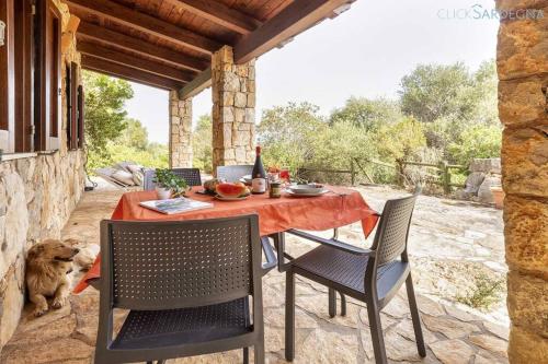 a table and chairs on a patio with a dog at Olivastri Cottage with pool in the Nature Park of Porto Conte in Santa Maria la Palma