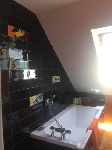 La salle de bains est pourvue d'un lavabo et d'un mur en carrelage noir. dans l'établissement Loue mancelle typique Le Mans Gare, au Mans