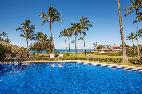 a swimming pool with palm trees and the ocean at Manualoha 901 Minutes to Poipu in Koloa