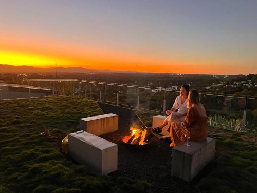 two people sitting around a fire on top of a hill at The Opal at Coolum - Mountain and Ocean Views in Yaroomba