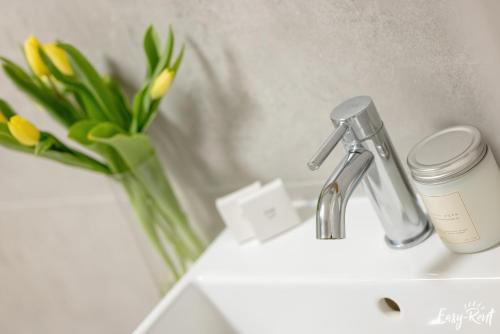 a bathroom sink with a faucet and a vase of flowers at Apartamenty Pinea z widokiem na morze Easy - Rent Apartments in Pobierowo