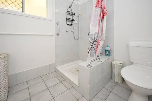 a white bathroom with a shower and a toilet at Groovy Beach Bungalow in Caloundra