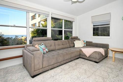 a living room with a brown couch and windows at Groovy Beach Bungalow in Caloundra