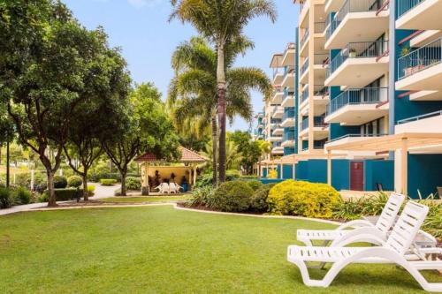 two white benches in the grass in front of a building at Alex Beachfront Apartment in Alexandra Headland
