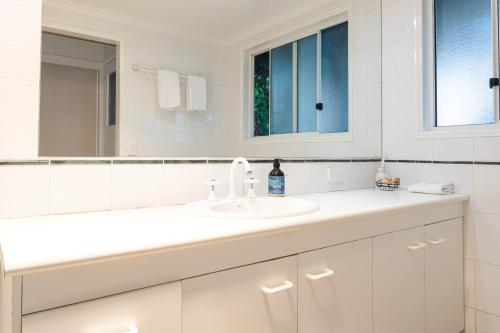 a white bathroom with a sink and a mirror at Moffat Beach Retreat, Pet-friendly & Ocean Views in Caloundra