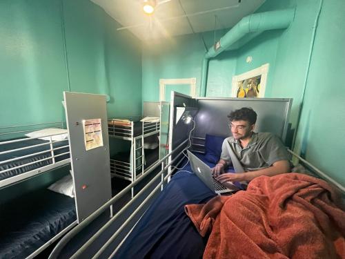 a man sitting on a bed with a laptop at Gaslamp Hostel in San Diego