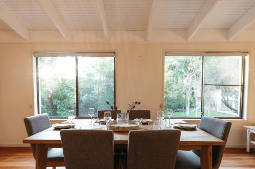 a dining room with a table and chairs and windows at Roderick Beach House Pet Friendly in Caloundra