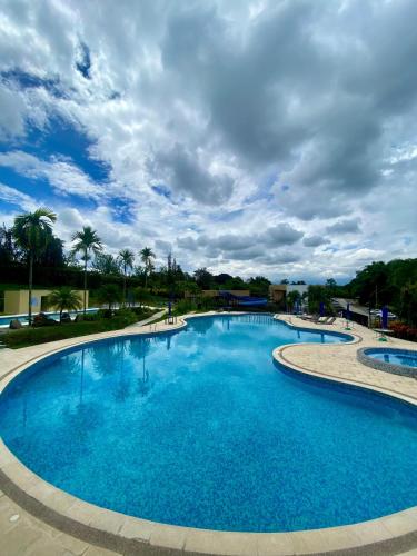 a large blue pool with palm trees and a cloudy sky at Apartasol Reserva de la Colina Lindo y Cómodo Apartamento in La Tebaida