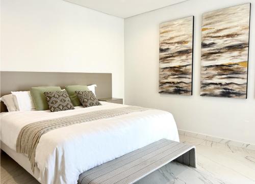 a white bedroom with a bed and two paintings on the wall at Peace of Mind - Las Brisas in Koolbaai
