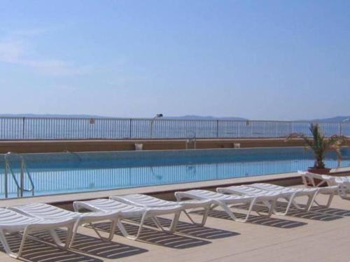 une rangée de chaises longues blanches à côté d'une piscine dans l'établissement T2 avec piscine collective et parking à Bormes-les-Mimosas - FR-1-803-12, à Bormes-les-Mimosas