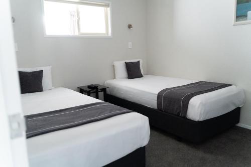 two beds in a room with white walls and a window at Pacific Coast Motor Lodge in Whakatane