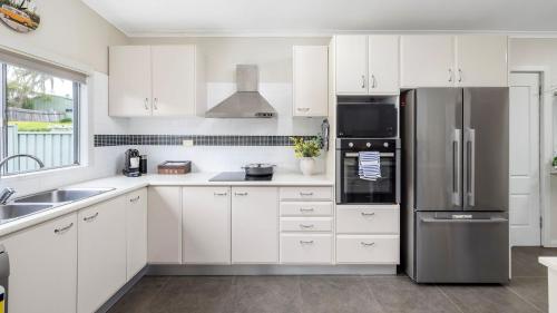 a kitchen with white cabinets and a stainless steel refrigerator at Shoal Sanctuary in Nelson Bay