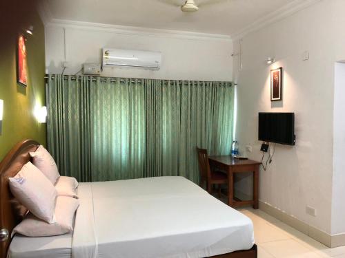 a bedroom with a white bed and a television at Hotel Nandanam in Guruvāyūr