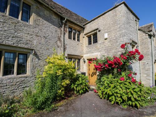 a brick building with red flowers and a door at Rood Cottage in Burford