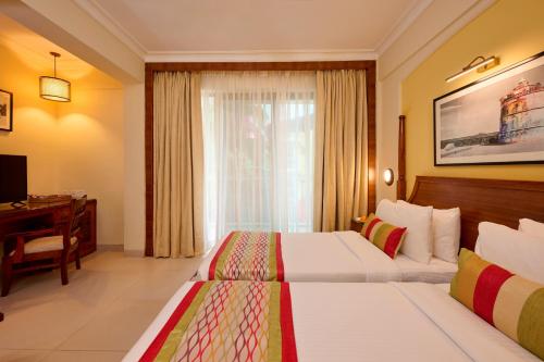 a bedroom with two beds and a desk and a window at Sea Breeze Sarovar Portico Varca Goa in Varca
