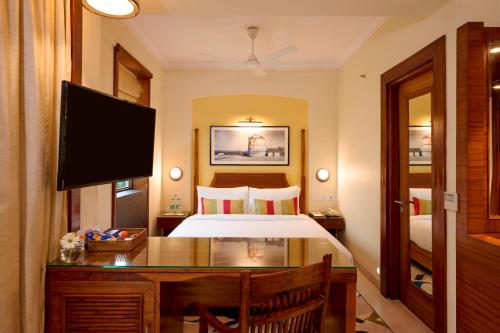 a bedroom with a bed and a desk with a television at Sea Breeze Sarovar Portico Varca Goa in Varca