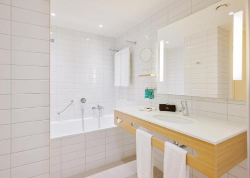 ein weißes Badezimmer mit einem Waschbecken und einer Badewanne in der Unterkunft Lufthansa Seeheim - More than a Conference Hotel in Seeheim-Jugenheim