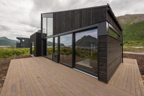 a house on a wooden deck with large windows at Hoda Cabin - Luxury lodge with jacuzzi and sauna in Lyngværet