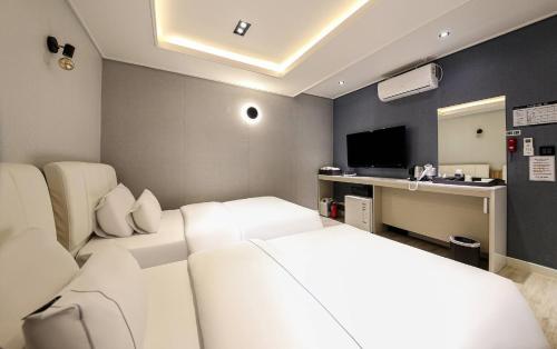 a bedroom with two beds and a desk with a television at Heimish Hotel in Tongyeong
