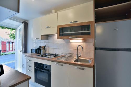 une cuisine avec des armoires blanches, un évier et un réfrigérateur dans l'établissement Gîte ker mamie - Maison 1km plage, Saint-Lunaire, à Saint-Lunaire