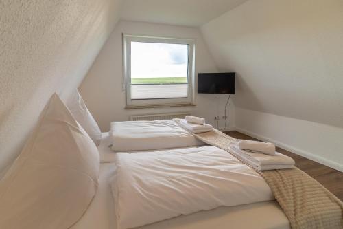 a bedroom with two white beds and a window at Deichblick No1 in Krummhörn